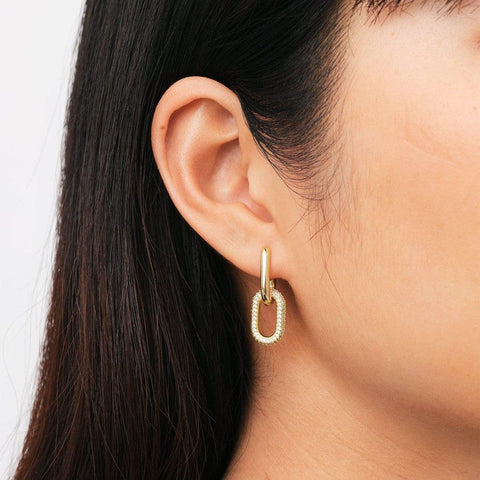 Chunky gold-plated brass link earrings featuring a sparkling crystal-encrusted drop design on a model.