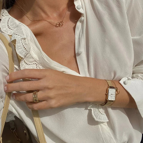 Elegant gold Daniel Wellington Elan Unity bracelet worn on a wrist alongside a matching gold watch and necklace.