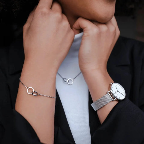 Elegant silver stainless steel Elan Unity bracelet featuring two interlocking rings on a delicate chain, worn with a matching watch.