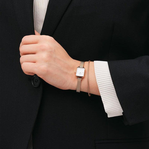 Elegant rose gold mesh bracelet paired with a matching Daniel Wellington watch on a wrist, styled with a black blazer.