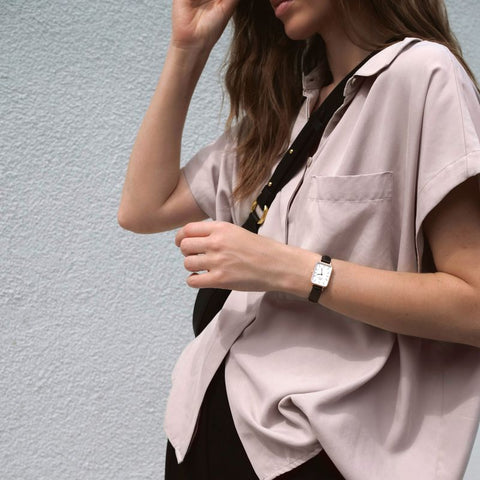 Daniel Wellington Quadro rose gold watch with a square white dial and black leather strap on a woman's wrist.