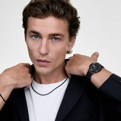 Unisex Daniel Wellington black stainless steel mesh necklace worn with a matching black mesh watch.