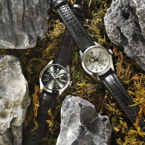 Seiko 5 Sports 36mm field watches with green and cream dials, stainless steel cases, and black leather straps on mossy rocks.